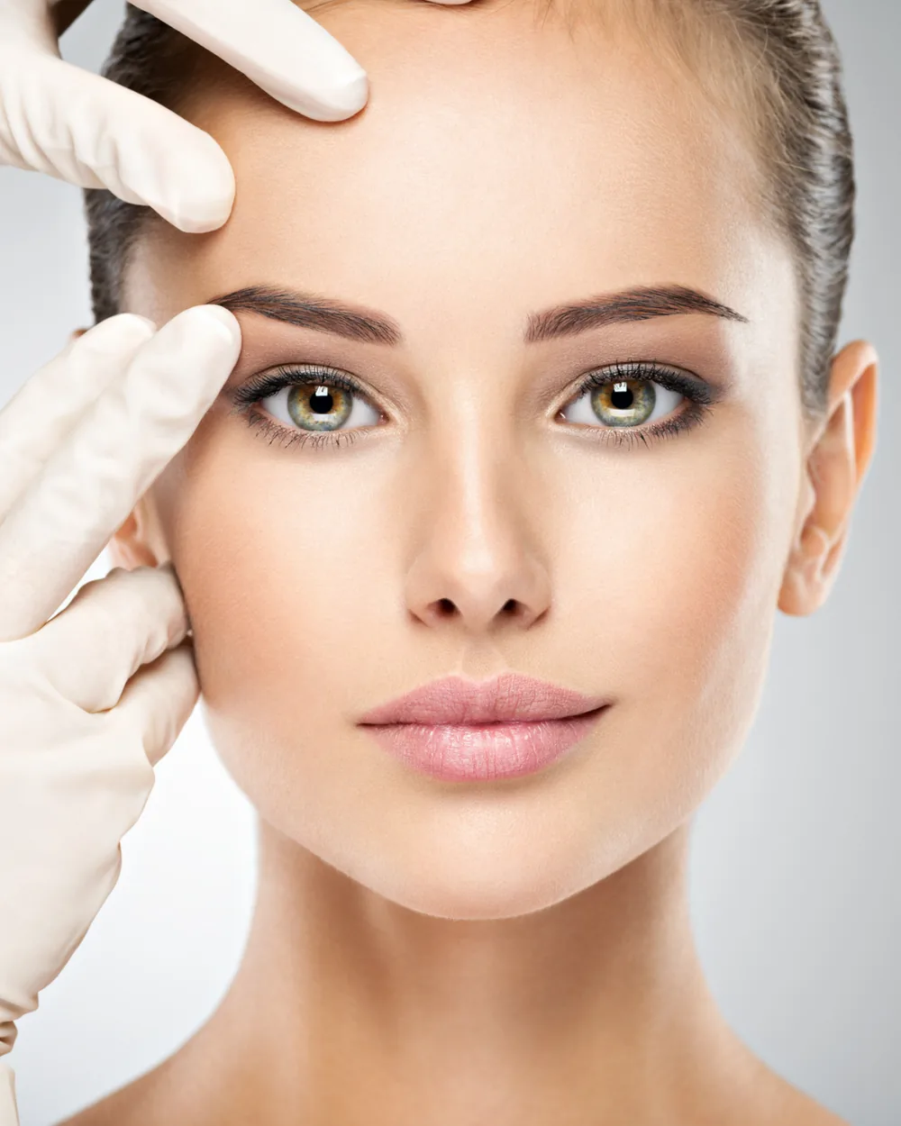 Gloved hands assessing the brow and periorbital region during a facial surgery consultation