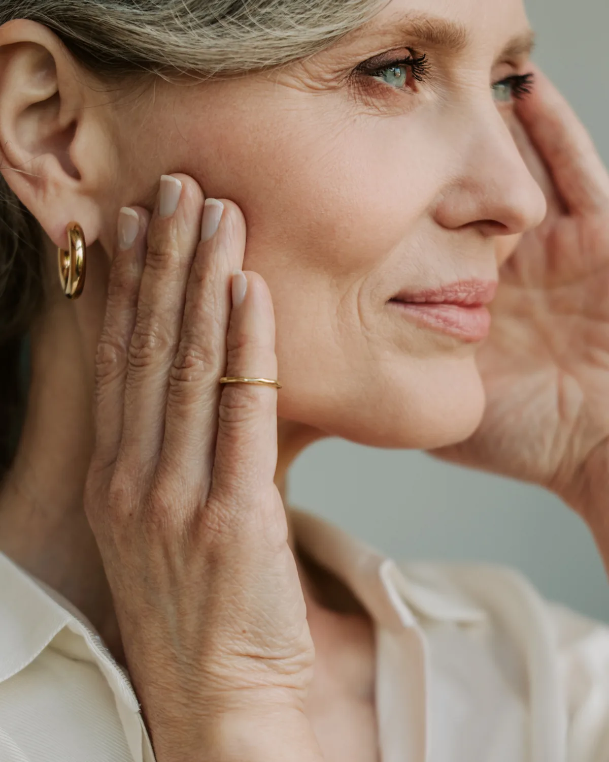 A woman in her sixties resting a hand along her jawline, illustrating the areas addressed by Comprehensive Facial Rejuvenation